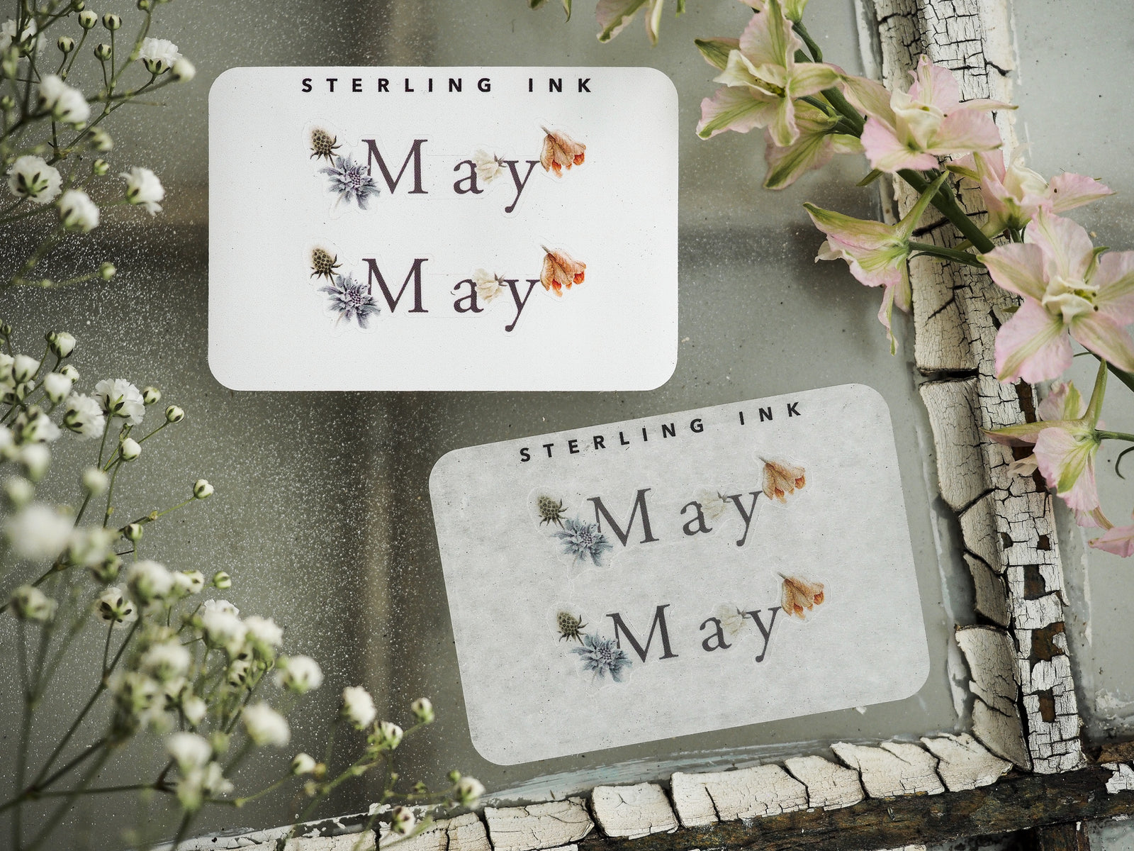 Minimalist May journaling stickers featuring the name "May" and "STEARLING INK" printed above delicate blue and peach botanical floral accents.