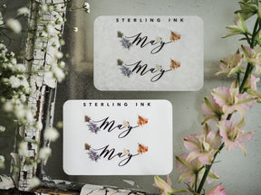 Two white monthly stickers for May, featuring the script word "May" decorated with delicate floral clusters of lavender and peach accents.
