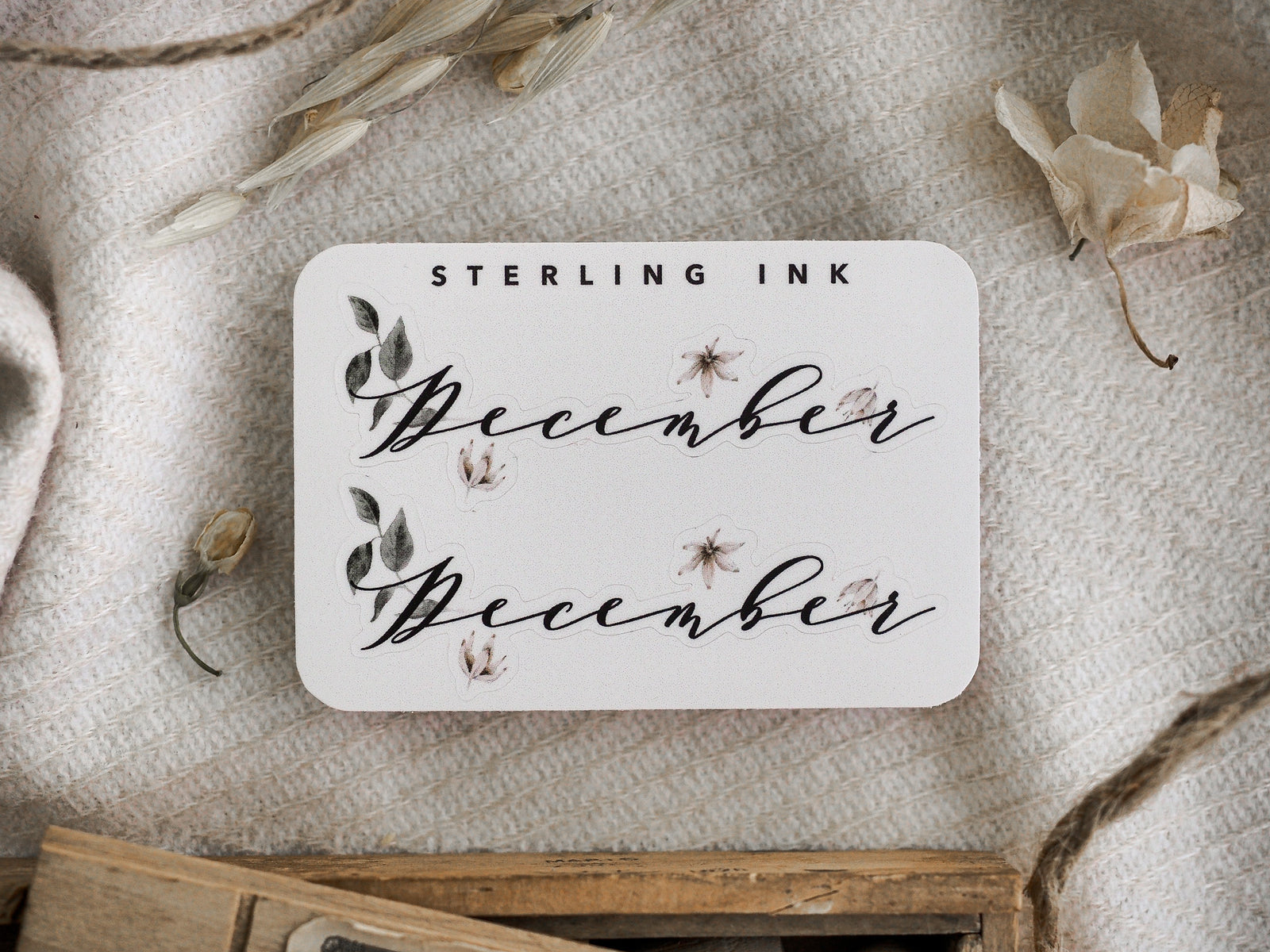 Elegant sticker set reading "December," decorated with fine script lettering and pale blush floral and leaf accents for seasonal planning.