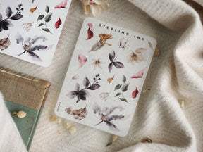 Botanical sticker sheet displaying watercolor illustrations of delicate autumn leaves, small flowers, and dried botanical elements in muted, earthy tones.