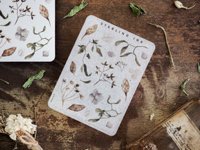 A sticker sheet displaying detailed botanical elements, including delicate leaves, small flowers, and stems, printed in muted earthy tones of green and brown.