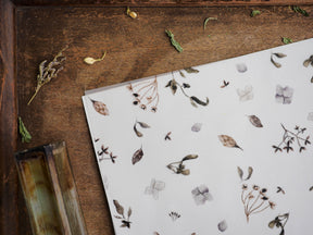 Earthy vellum sheet featuring a delicate, scattered botanical print of dried foliage, small flowers, and stems in muted brown and gray tones.