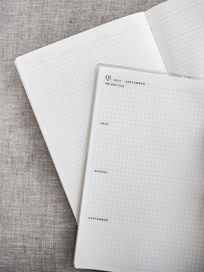 Undated, open planner spread displaying pale graph paper grid lines and clearly marked monthly headers for scheduling and general organization.