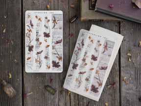 Vintage washi sticker strips with a botanical theme, featuring sepia-toned illustrations of dark red and brown flowers printed over antique-style scientific text.