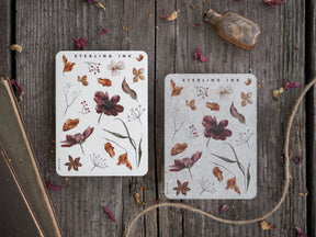 Two decorative stickers featuring detailed autumnal botanical elements, including brown leaves, small white flowers, and delicate plant arrangements on a white background.